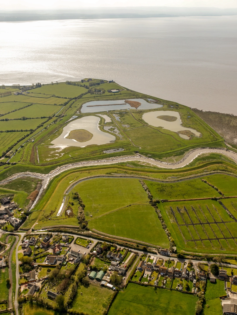 Golygfa o’r awyr o dirwedd werdd a dyfrffyrdd ger afon.