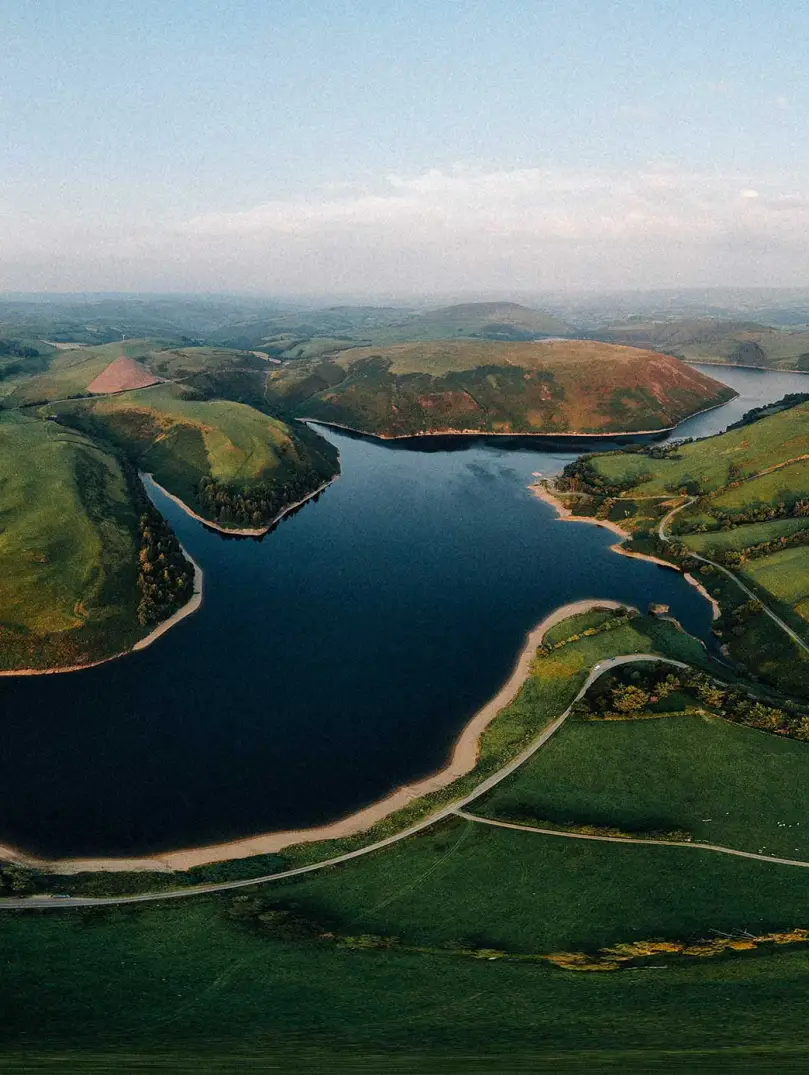 panorama o gronfa wydr a bryniau gwyrdd gyda'r haul