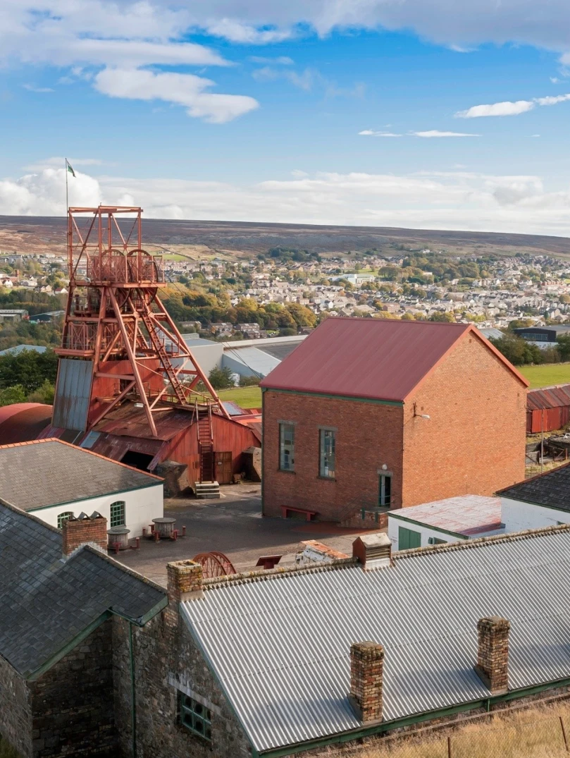 Golygfa o siafft godi ac adeiladau Pwll Mawr gyda'r dref yn y cefndir  