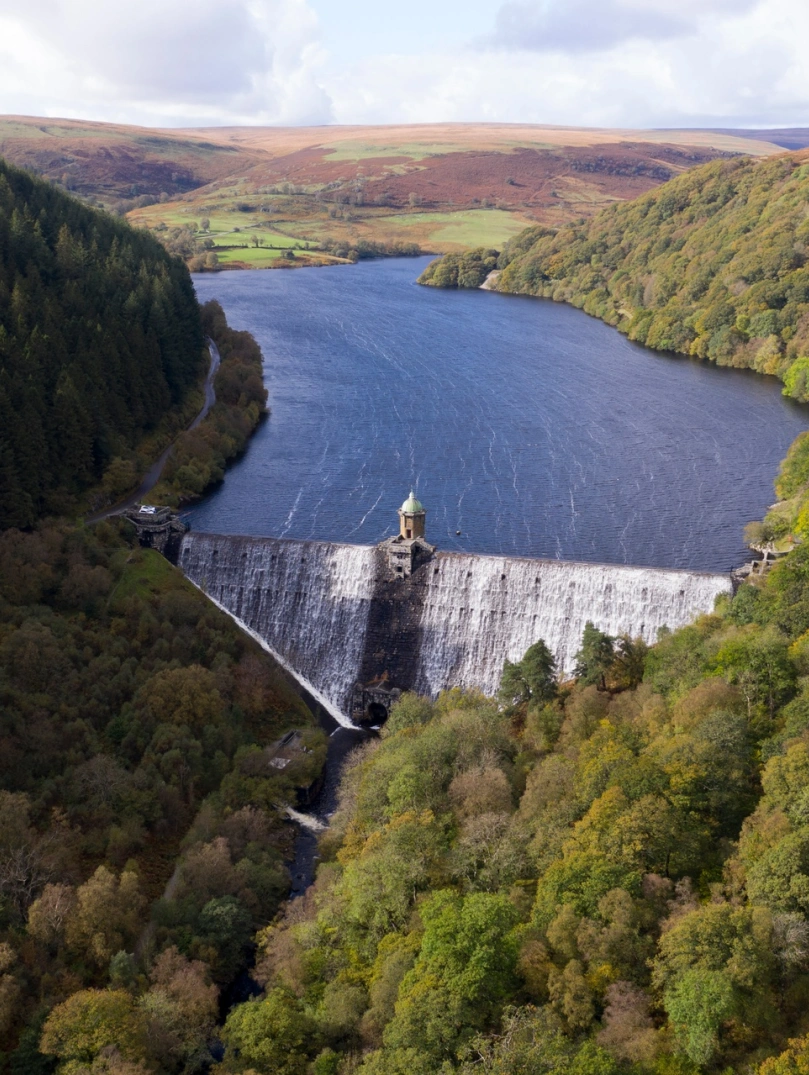 Llun o'r awyr o'r afon a ddaliwyd yn ôl gan yr argae wedi'i amgylchynu gan goedwig.