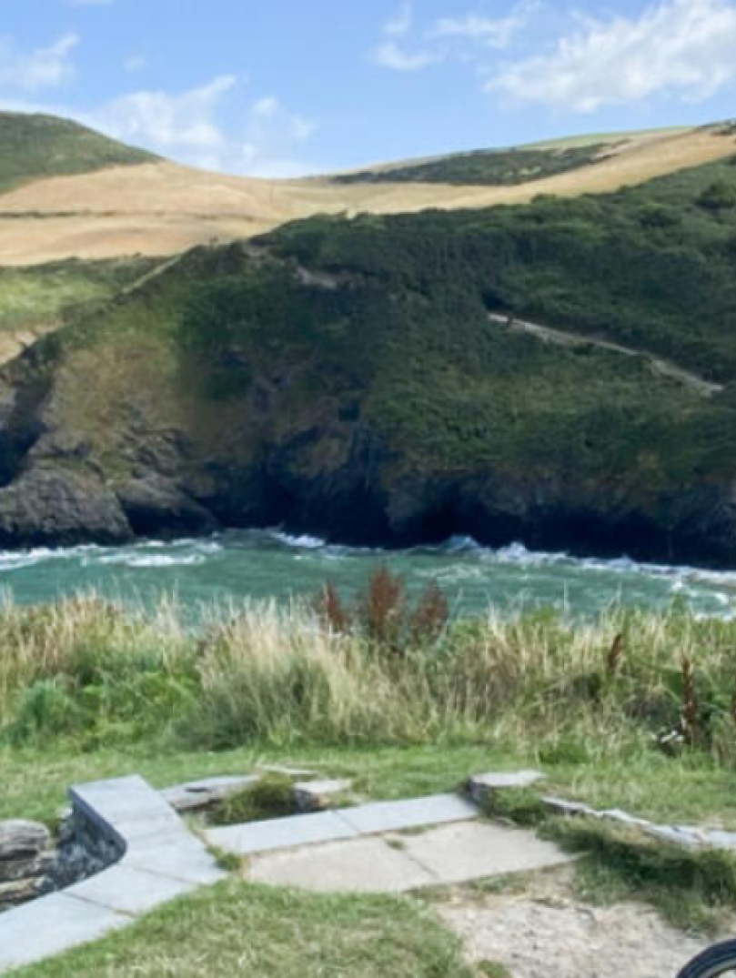 Person yn sefyll gyda beic yn edrych allan dros y môr