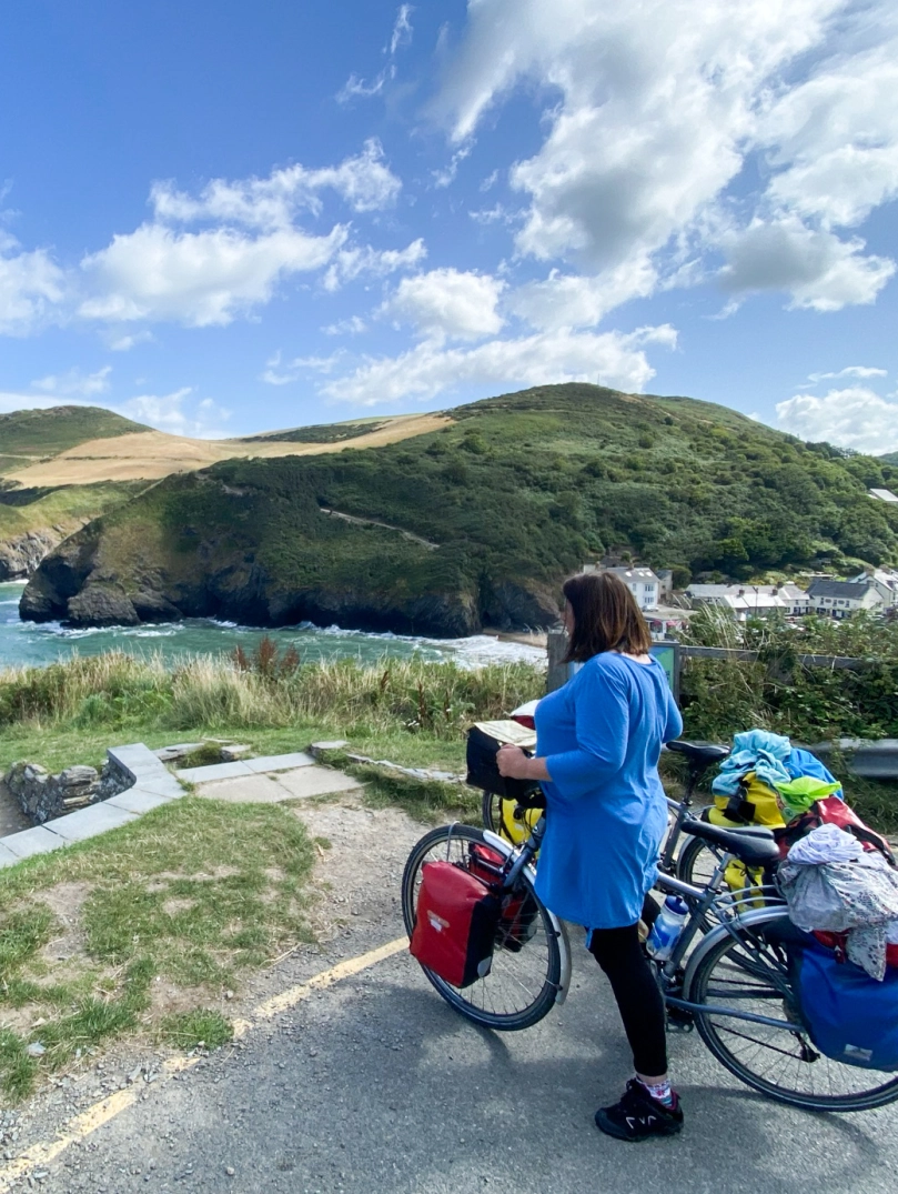 Person yn sefyll gyda beic yn edrych allan dros y môr