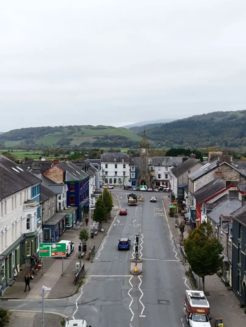 Golygfa awyr o Heol Maengwyn ym Machynlleth, gyda bryniau yn y cefndir.