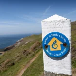 Arwyddbost ar lwybr yr arfordir yn edrych dros ddŵr.