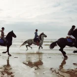 Tri person yn marchogaeth ar y traeth 