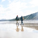 Dau yn cerdded ar y traeth ym Mhorth Dinllaen. 