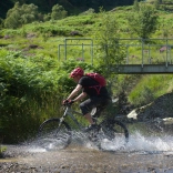 Beiciwr yn torri trwy afon yng Ngheredigion
