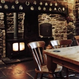 Bwrdd mewn tafarn o flaen tân go iawn wedi ei adeiladu i mewn i’r wal gerrig.