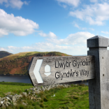Arwydd Llwybr Glyndŵr gyda Llyn Clywedog a bryniau yn y cefndir