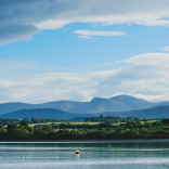 Llun o'r môr gyda choed a bryniau yn y pellter.