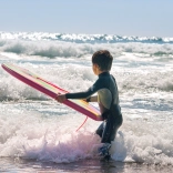 Plentyn yn sefyll yn y môr yn dal bodyboard
