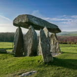 Llun o gerrig y siambr gladdu mewn cae gyda bryniau yn y pellter