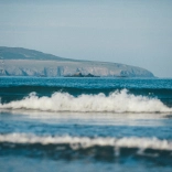 Llun gydag Ynys Dewi yn y cefndir, a'r môr a thonnau yn y tu blaen