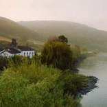 Adeilad gwyn ar lan yr afon, gyda bryniau yn y cefndir