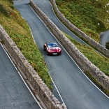 Llun o'r awyr o gar Aston Martin coch yn gyrru ar hyd ffordd