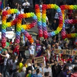 Torf o bobl yn gafael mewn balŵns sy’n dweud Pride.