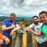Four men doing a thumbs up sign at stone marker in Llanwono forestry after trail running.