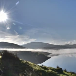 Rhywun yn edrych dros y mynyddoedd a llyn yn gynnar yn y bore.