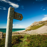 Arwydd llwybr arfordir Cymru gyda thwyni tywod a'r môr yn y cefndir