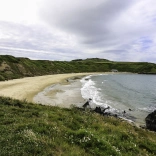 Dyn yn edrych draw ar draeth o dywod euraidd. 