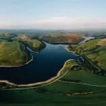 panorama o gronfa wydr a bryniau gwyrdd gyda'r haul
