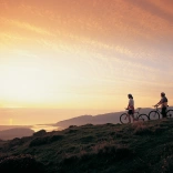 Dau berson gyda beic mynydd yn edrych ar yr haul yn machlyd yn  aber afon Mawddach eastuary.