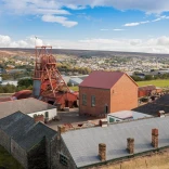 Golygfa o siafft godi ac adeiladau Pwll Mawr gyda'r dref yn y cefndir