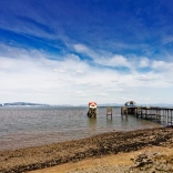 Pier yn mynd allan i'r môr gydag awyr las yn gefndir. 