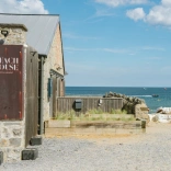 Tu allan bwyty Beach House yng Ngŵyr gyda'r môr yn y cefndir.