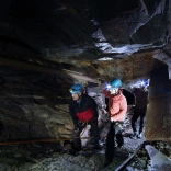 Grŵp o bobl yn gwisgo helmedi yn cerdded ar lwybr tanddaearol mewn chwarel lechi.