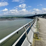 Edrych i lawr pier hir arddull Fictoraidd gyda'r pentir a'r môr yn y pellter.
