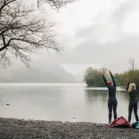 Tri ffrind yn nofio mewn dŵr oer yn Llyn Padarn, Parc Cenedlaethol Eryri (Eryri), Gogledd Cymru