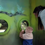 Bachgen bach a menyw yn edrych drwy ffenestri crwn ar bysgod mewn sŵ.