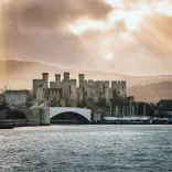 Castell anferth gyda thyrau a muriau enfawr ger marina, gydag awyr gymylog uwchben.