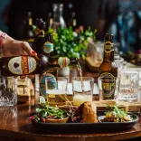 Platiad o fwys setil tapas a photel brown o Wrexham Lager yn cael ei roi mewn gwydr.