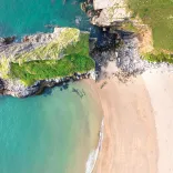 Traeth tywodlyd euraidd gydag ychydig o greigiau yn ymwthio i fôr gwyrddlas.