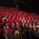 Cynulleidfa yn eistedd mewn cadeiriau coch y tu mewn i awditoriwm sinema.