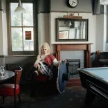 Catrin Feelings, y frenhines drag, yn eistedd mewn tafarn draddodiadol yng Nghymru.