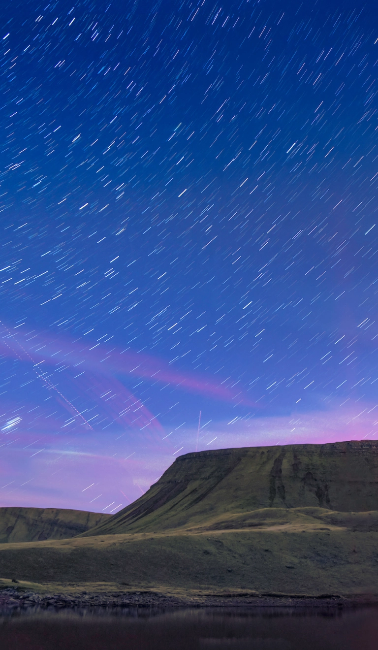 Llun o olion y sêr yn yr awyr, uwchben y llyn gyda mynyddoedd yn y cefndir