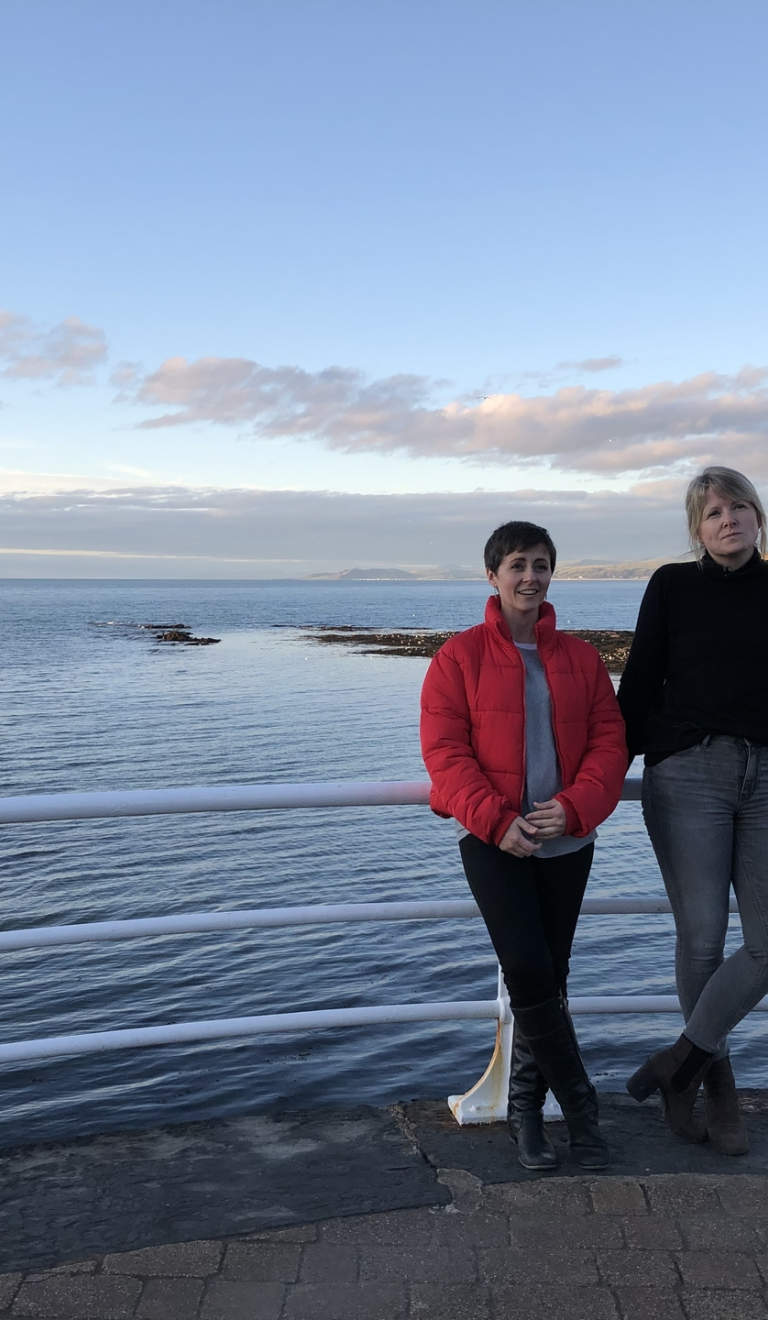 Two women in front of the sea with Constitution Hill in the background.