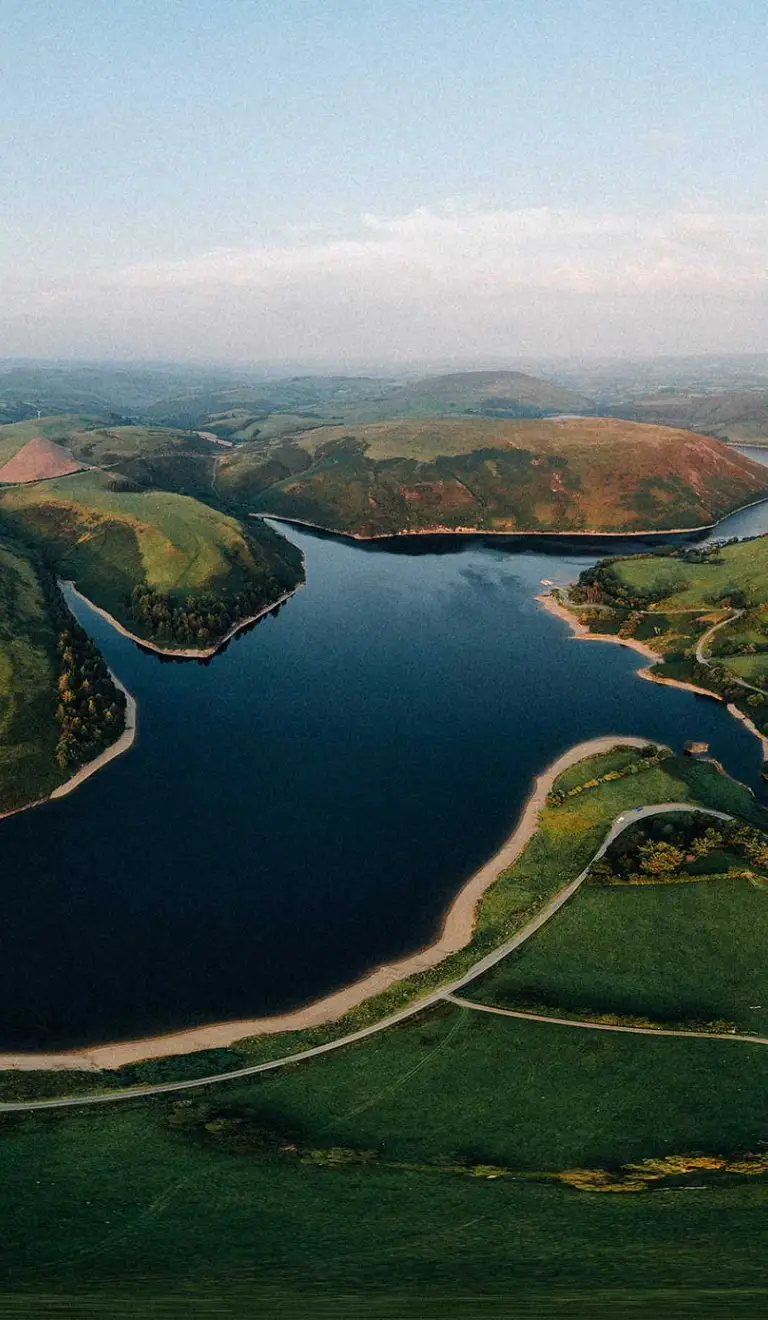 panorama o gronfa wydr a bryniau gwyrdd gyda'r haul