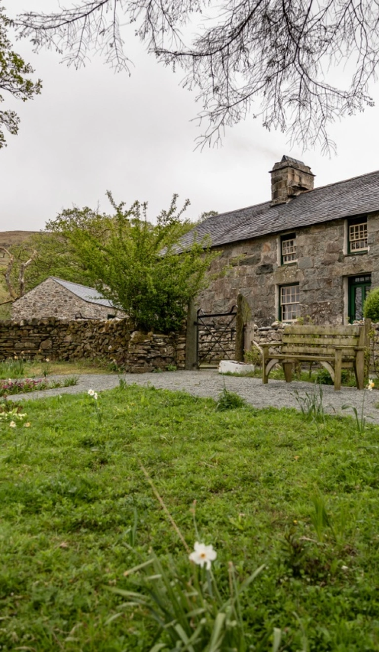 Tu allan i hen ffermdy carreg a gardd o'i flaen. 