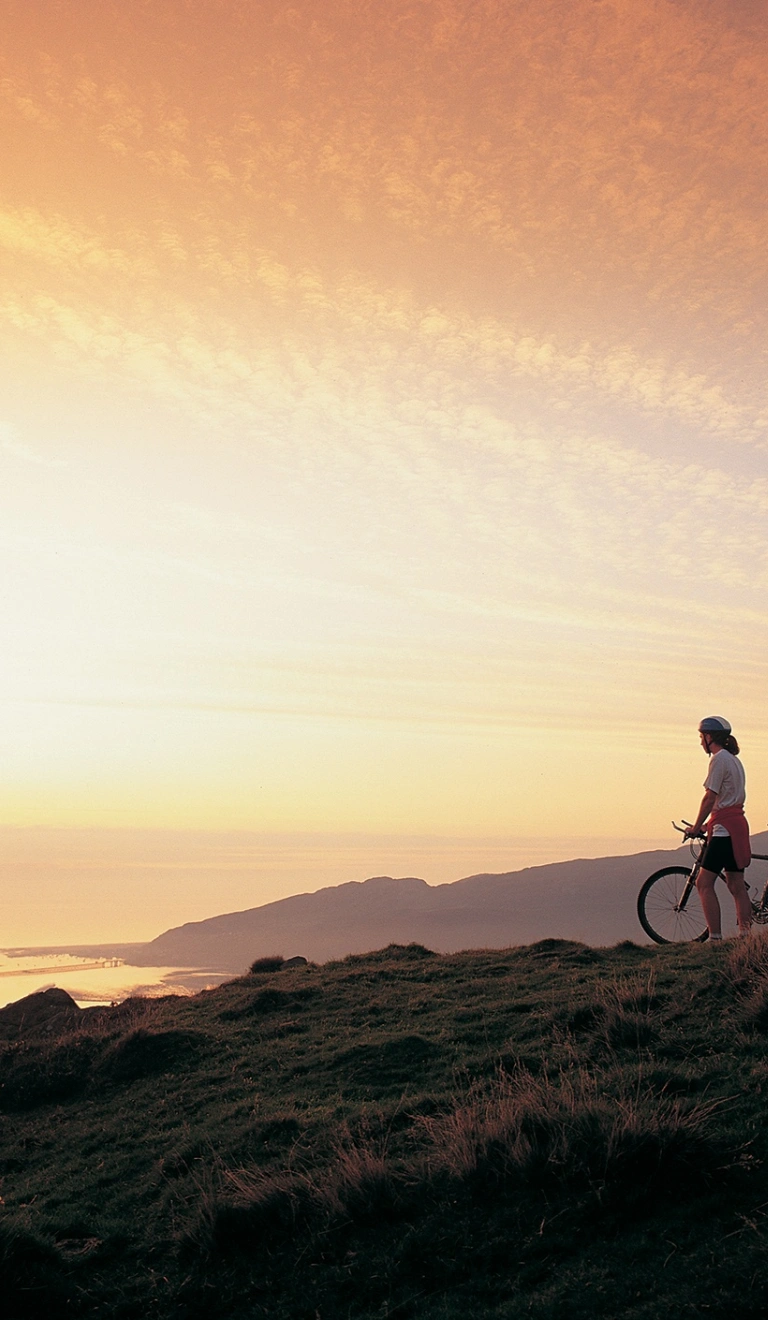 Dau berson gyda beic mynydd yn edrych ar yr haul yn machlyd yn aber afon Mawddach eastuary.