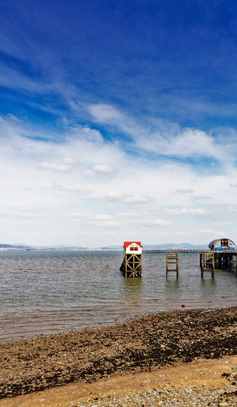 Pier yn mynd allan i'r môr gydag awyr las yn gefndir.