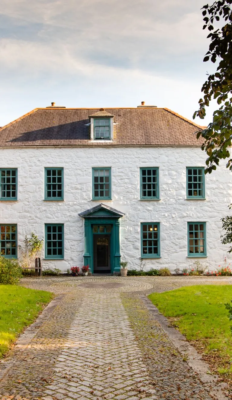 Llun o'r tu allan i dŷ mawr gwyn gyda llwybr a gatiau ar agor yn y tu blaen